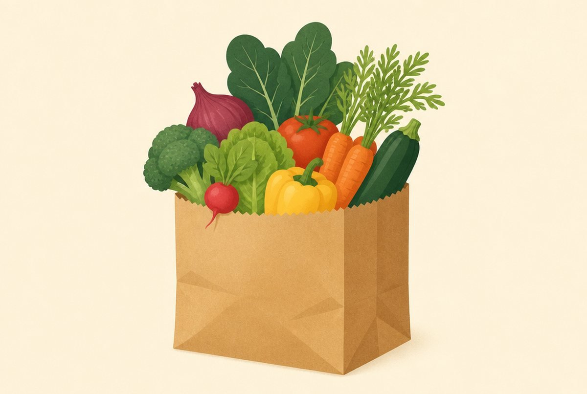 Brown paper grocery bag brimming with fresh vegetables: carrots, broccoli, peppers, leafy greens, tomato, radish, and zucchini.